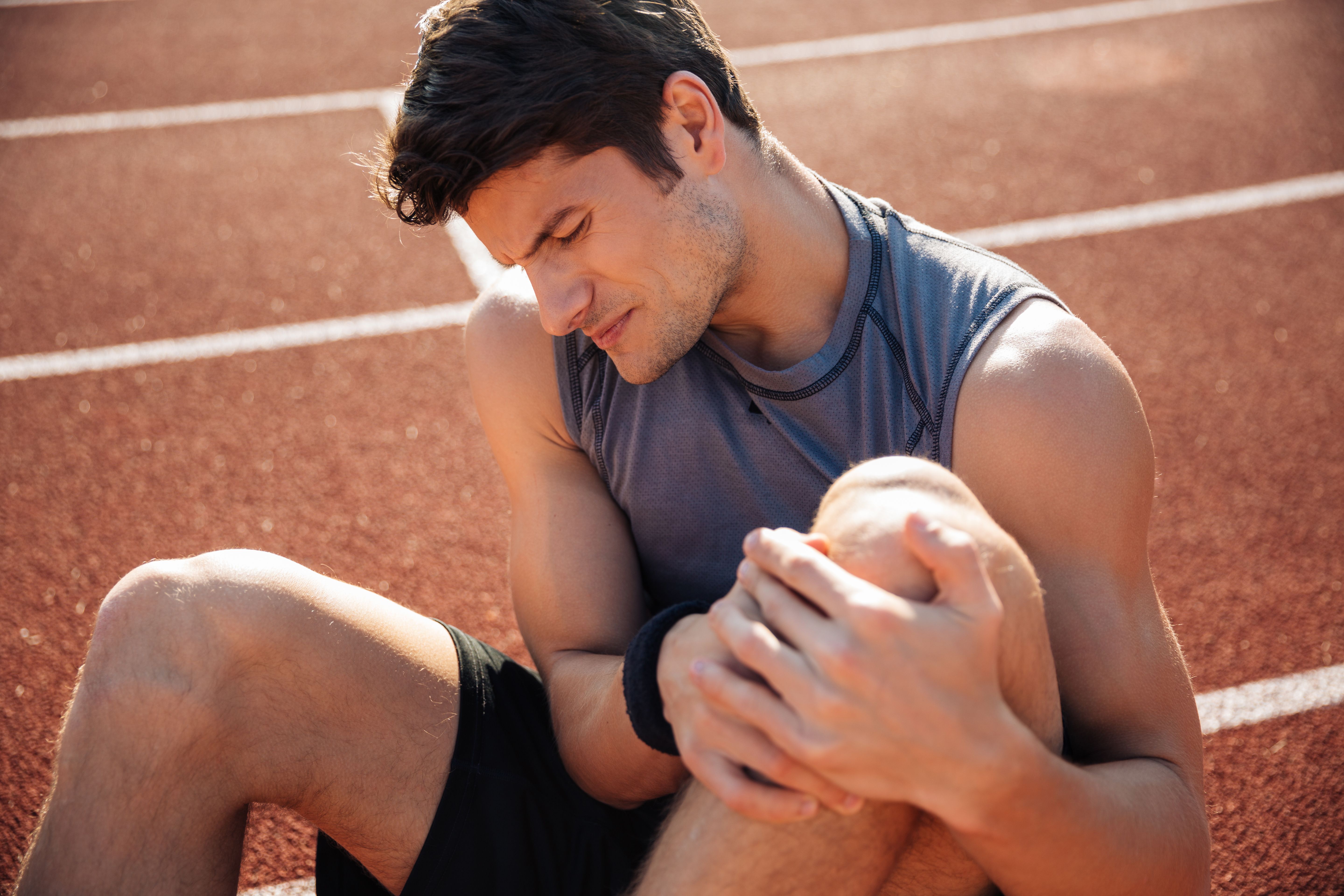 A man sitting down on a running track, holding his injured knee